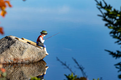 Man figurine fishing  on rock against blue lake