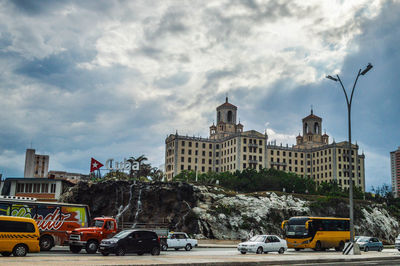 Cars on road by buildings in city against sky