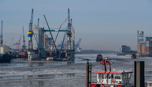 Cranes at harbor against sky