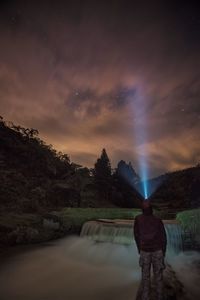 Man with illuminated headlamp standing by river against star field