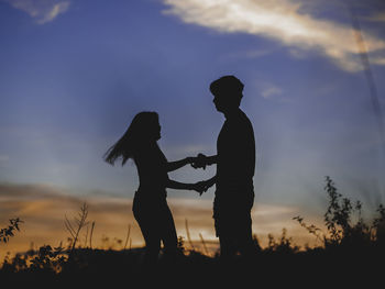 Silhouette couple standing on field against sky during sunset