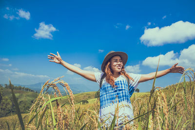 Smiling woman wearing hat standing on field against sky