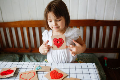Cute caucasian child with a card with a heart made of cardboard and threads. 