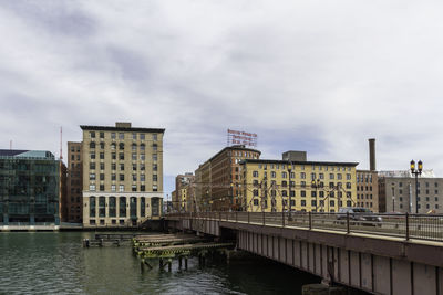 Bridge over river by buildings in city against sky