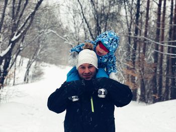 Portrait of smiling man with child standing at snow covered forest