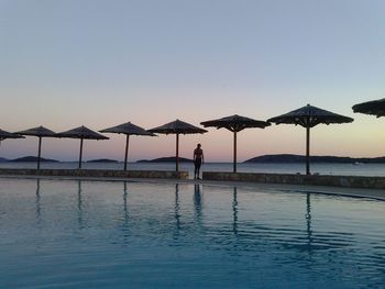 Rear view of woman standing in between infinity pool and sea at sunset