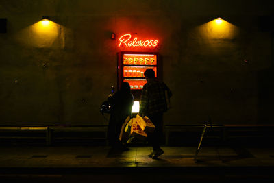 Rear view of man walking on illuminated sign at night