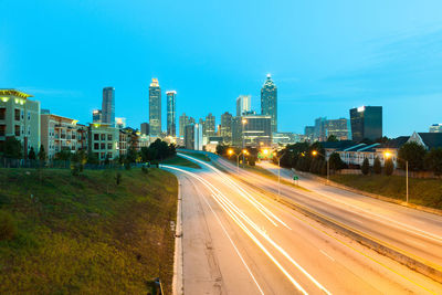 Light trails on road by buildings against sky in city