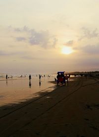 People at beach against sky during sunset