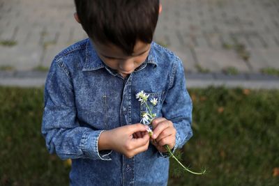 Boy holding flower while standing outdoors