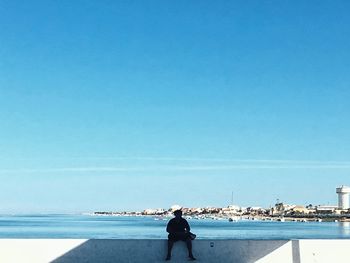 Rear view of man looking at sea against clear sky