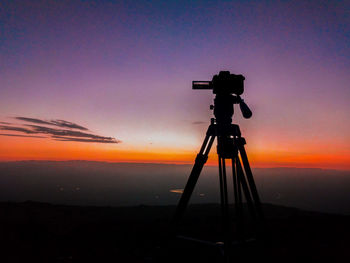 Silhouette of camera against sky during sunset