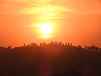 Silhouette group of people in desert against orange sky