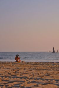People sitting on beach against clear sky during sunset