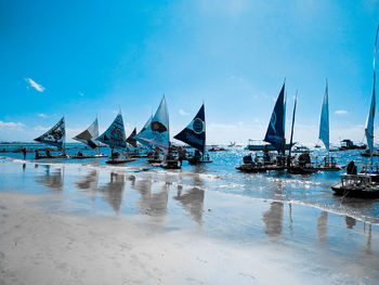 Sailboats moored on beach against blue sky