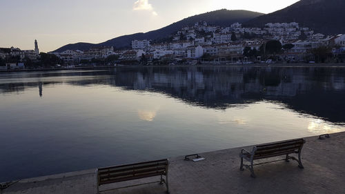 Lake by buildings in town against sky during sunset