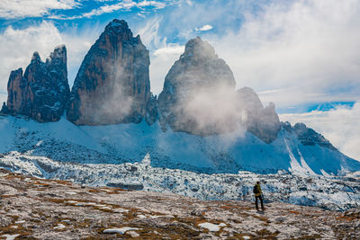 Rear view of boy standing by snow capped mountain against sky