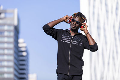 Man listening to music standing against building in city