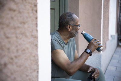 Thirsty senior man with bottle at doorway of house