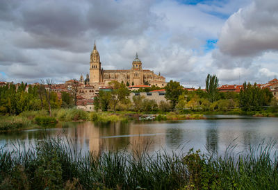 View of buildings by river against cloudy sky
