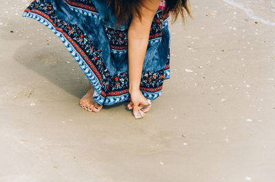 Low section of woman picking seashell at beach