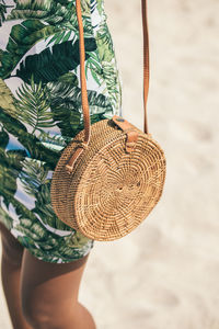 Girl walks along the beach with a rattan bag on her shoulder