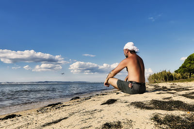 Man sitting on beach against sky