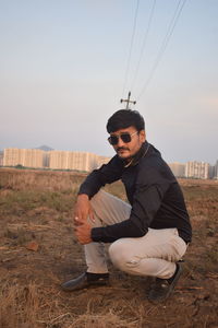 Young man sitting on land against sky