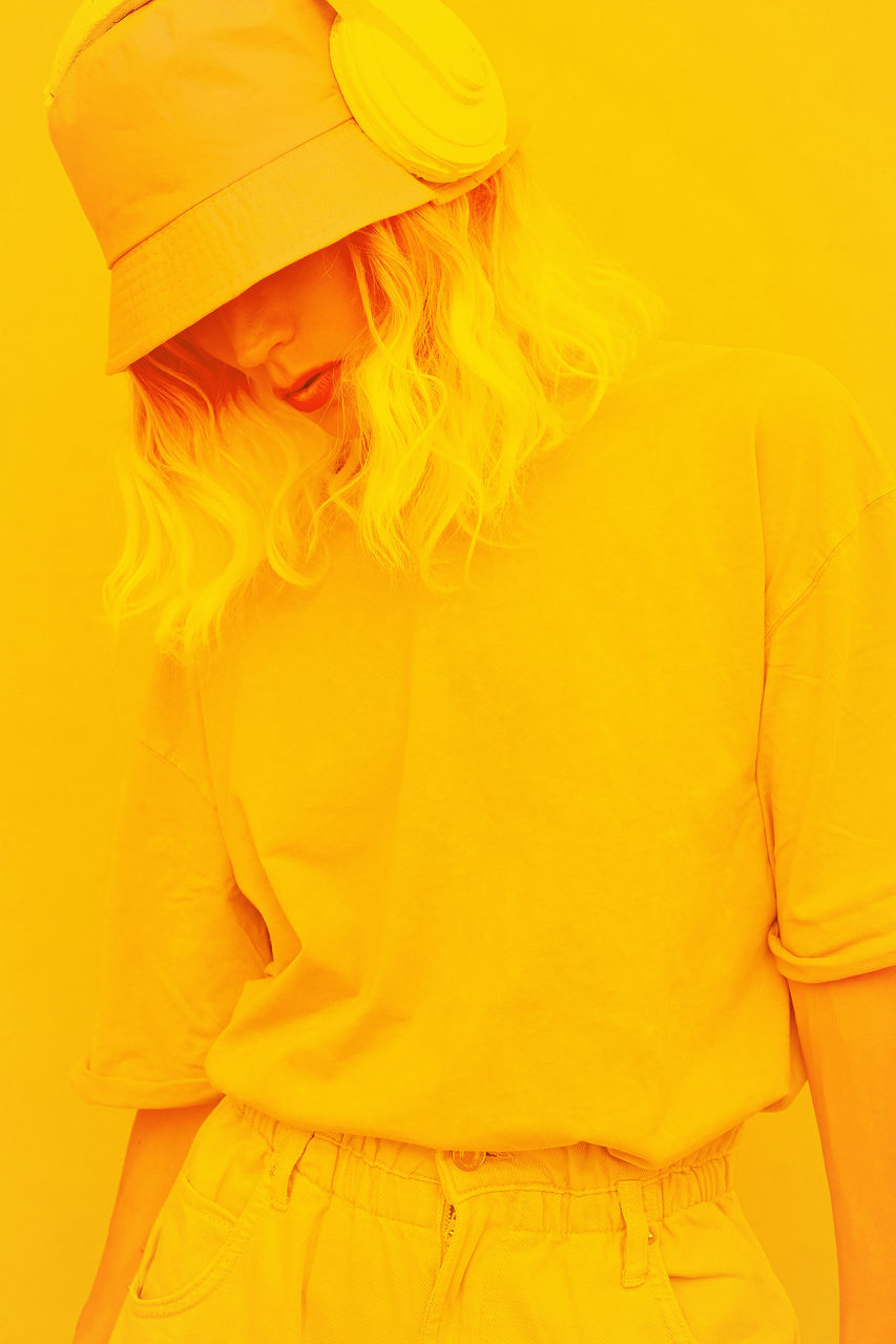 yellow, orange, clothing, one person, adult, women, studio shot, indoors, fashion, young adult, blond hair, waist up, portrait, yellow background, colored background, casual clothing, hat, hairstyle, front view, sleeve, fashion accessory, standing, female, long hair, three quarter length