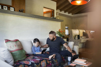 Father talking to son using tablet computer in living room