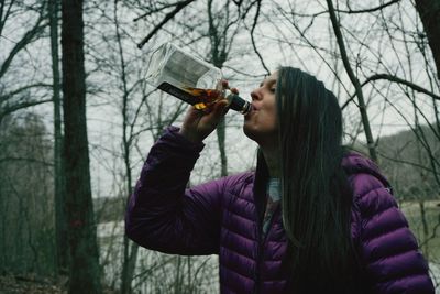 Young woman drinking water from glass of bare tree
