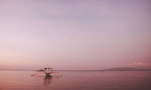 Outrigger boat sailing on lake against sky during sunset