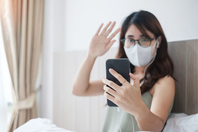 Close-up of woman wearing mask video calling on phone at home