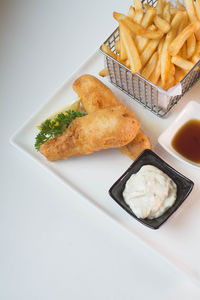 High angle view of fried fish and french fries in plate against white background