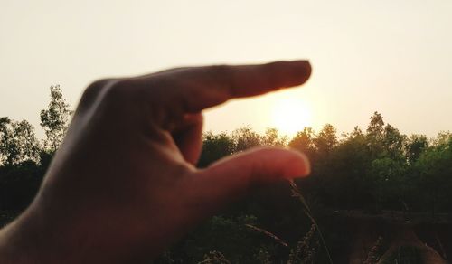Close-up of hands against clear sky during sunset