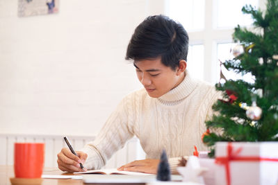 Man writing in book by christmas tree at home
