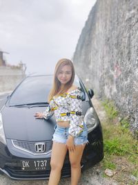 Portrait of smiling young woman standing on car