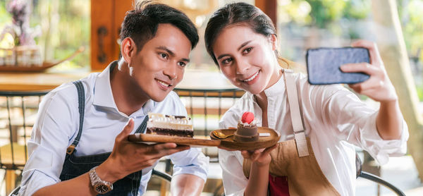 Cheerful couple holding cake while doing selfie