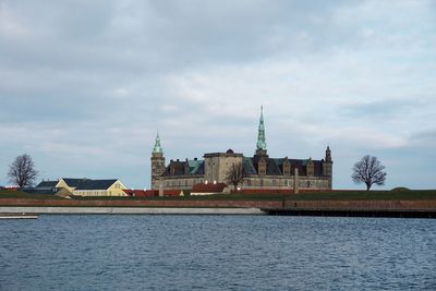 View of buildings by river against cloudy sky