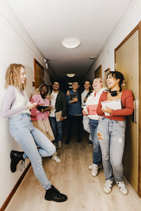 Multiracial students looking at female friend and laughing at corridor in college dorm
