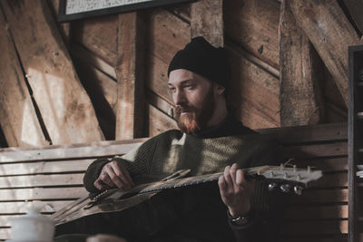 Young man looking away while sitting on wood