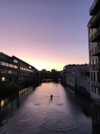 Silhouette buildings by canal against sky during sunset
