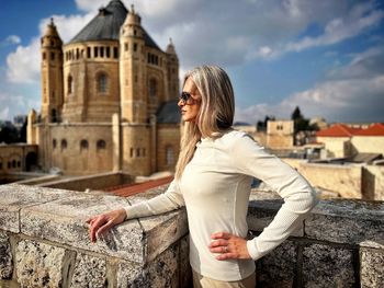 Side view of young woman standing against historic building