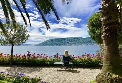 Rear view of woman sitting on bench against sky