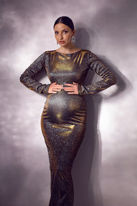 Trendy stylish beautiful pregnant woman in a tight silver sequined dress against a white wall 