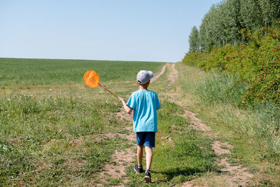 Cute boy catches butterflies with scoop-net on sunny meadow. young explorer of the nature.