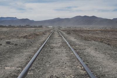 Railroad track leading towards mountains against sky