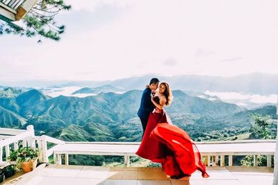 Young woman standing on railing against mountain range