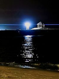 Illuminated bridge over sea against sky at night