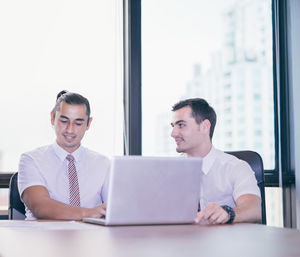 Young businessmen discussing over laptop against window at office